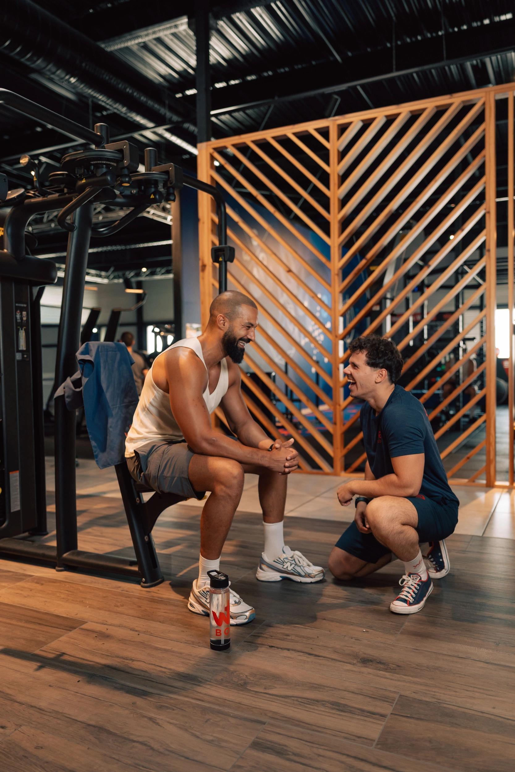 Deux hommes discutent dans une salle de fitness à Saint-Orens équipée de machines modernes