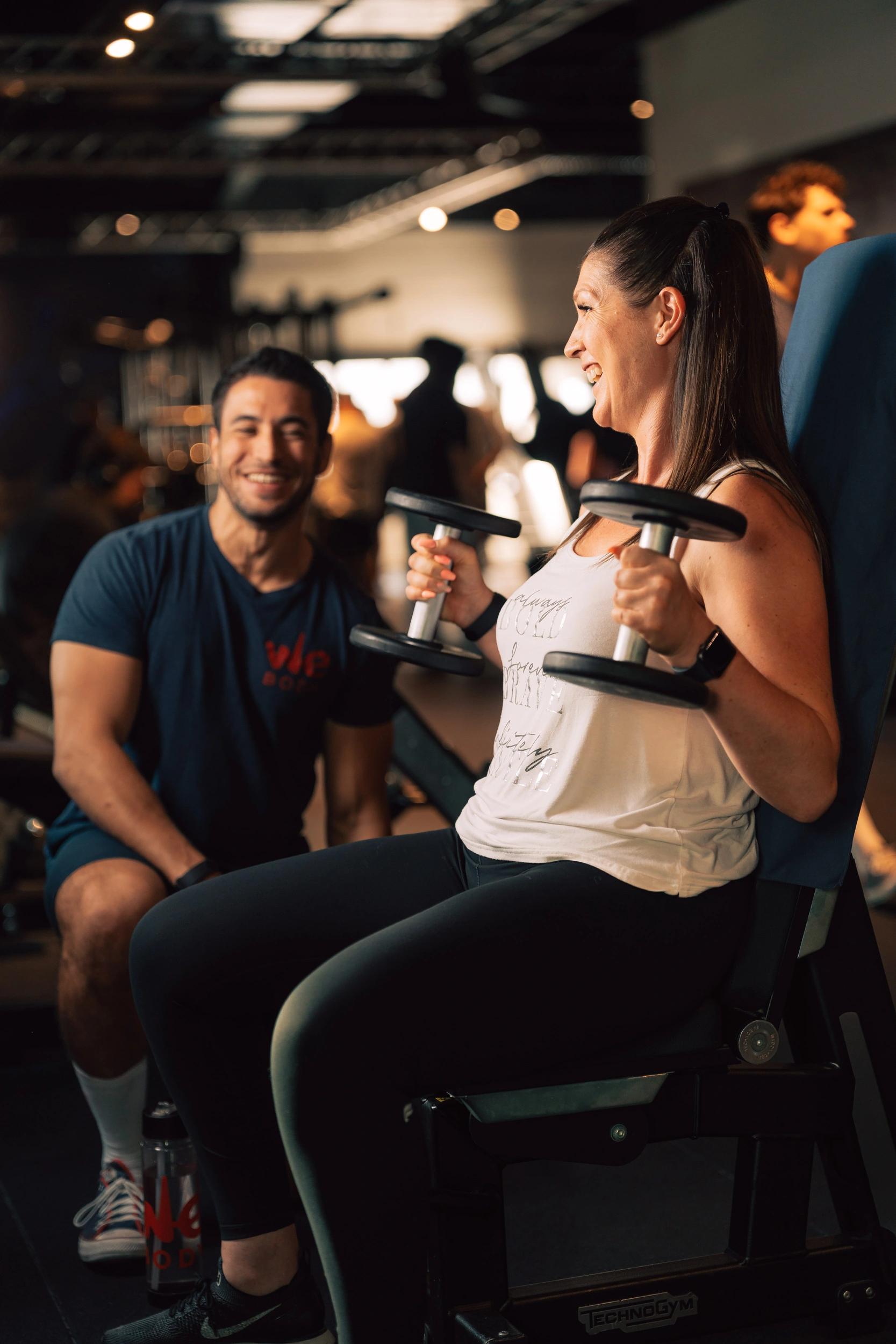 Femme souriante utilisant des haltères dans une salle de fitness à Saint-Orens avec un coach
