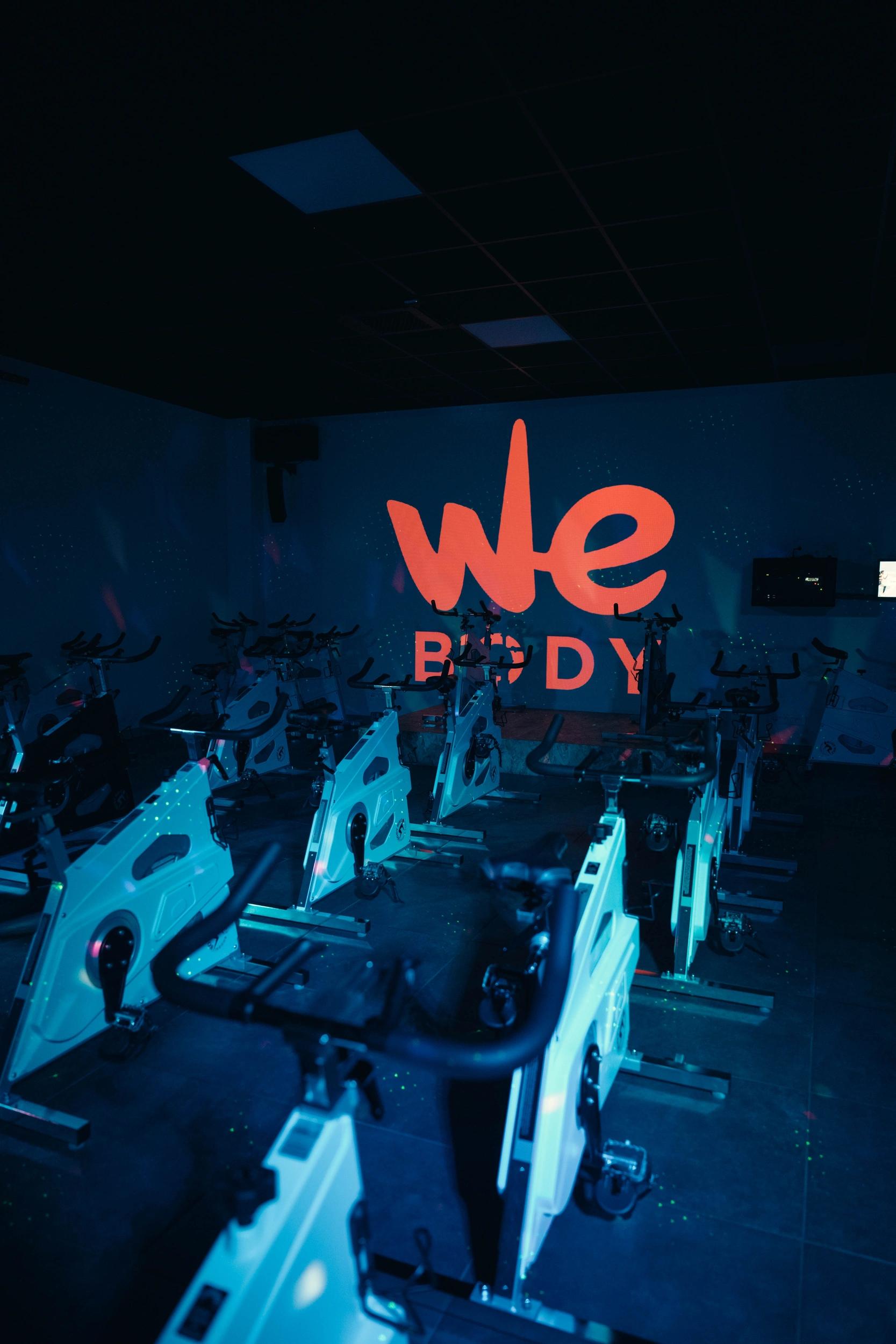 Salle de sport à Saint-Orens avec vélos fitness et logo We Body illuminé