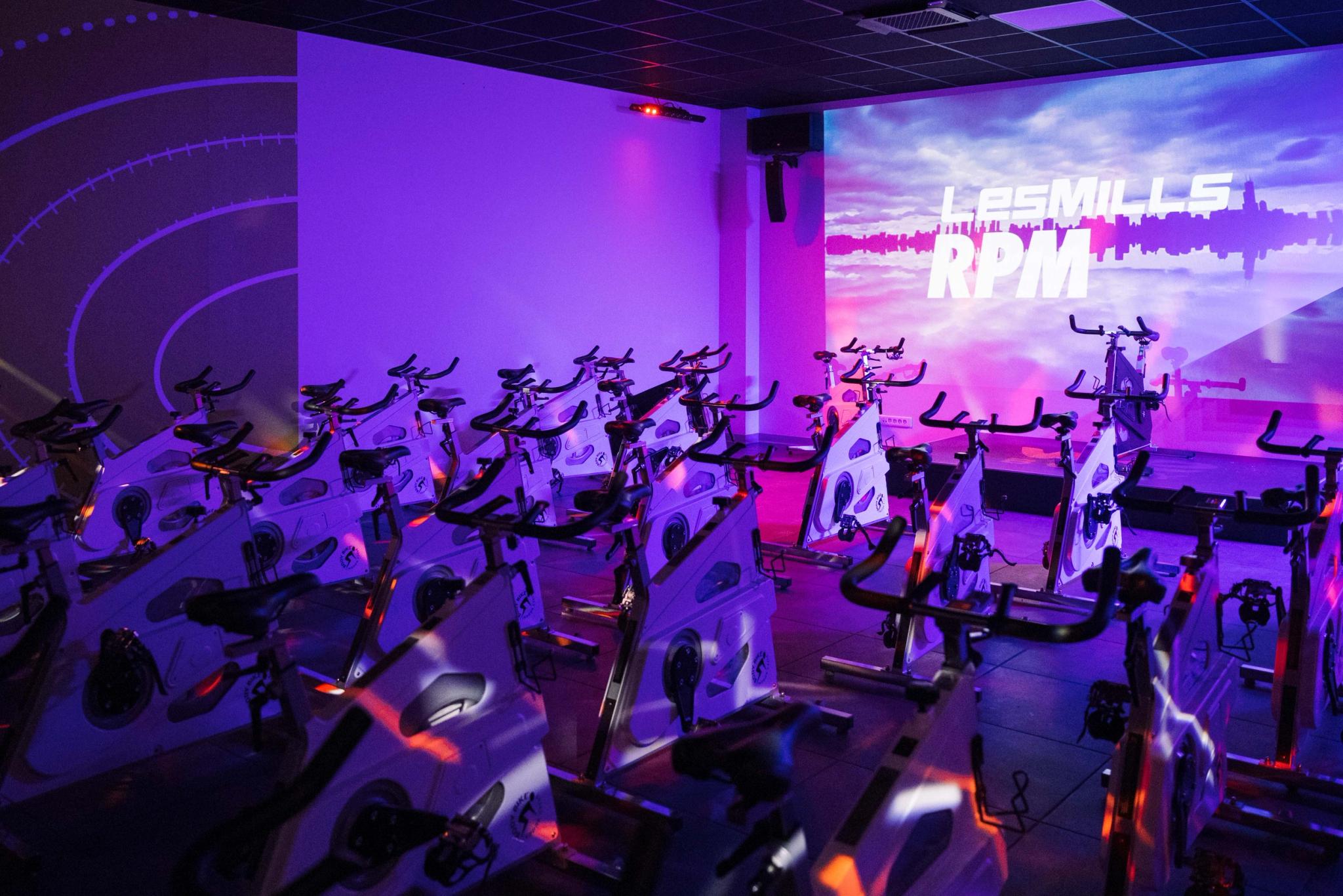 Salle de sport à Saint-Orens avec vélos de spinning sous éclairage LED violet futuriste