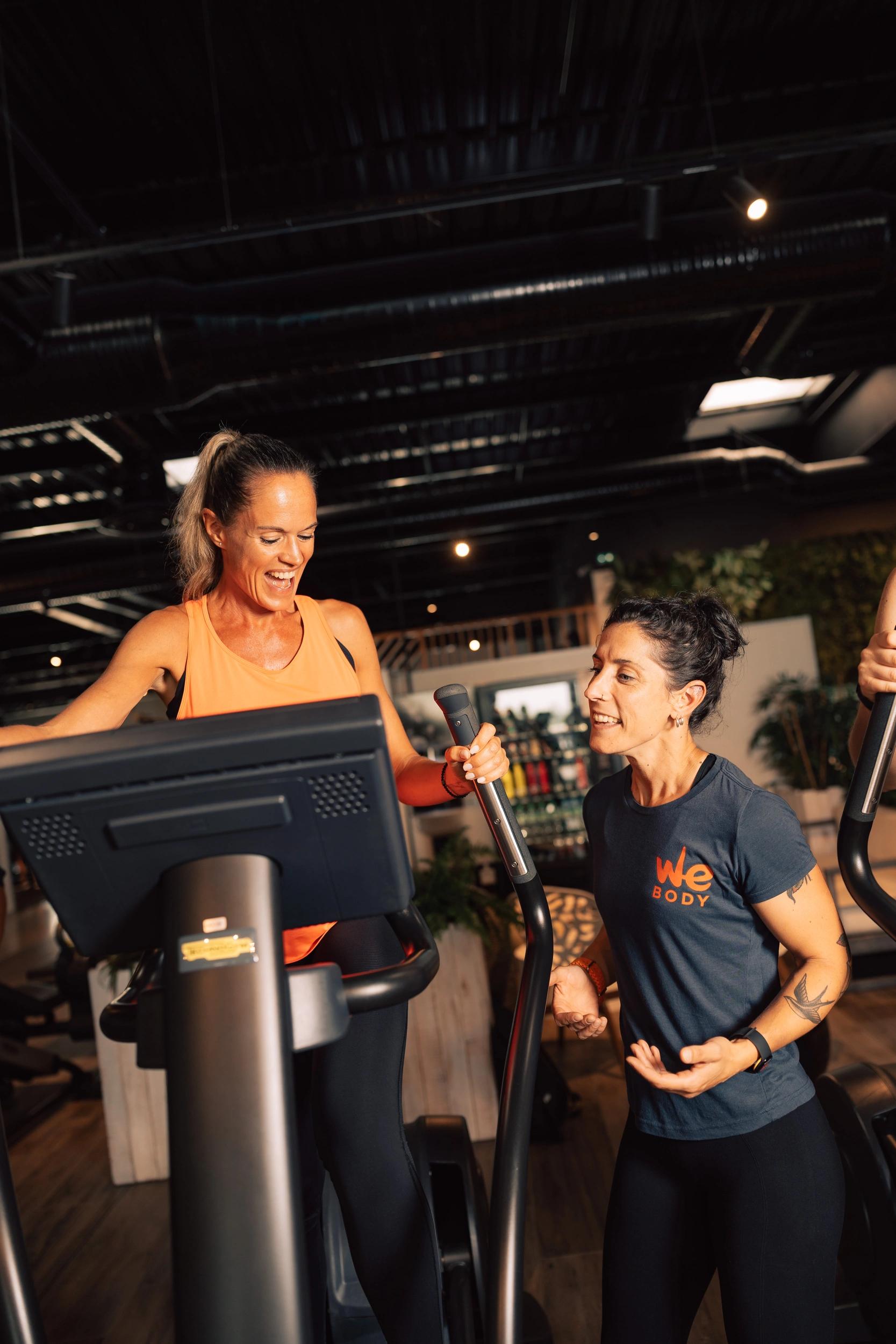 Deux femmes souriantes s'entraînent sur des vélos d'exercice dans une salle de sport à Saint-Orens